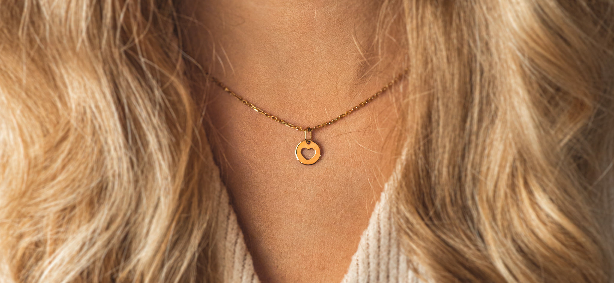 Pozłacany naszyjnik celebrytka, z okrągłą ażurową zawieszką z sercem. Symboliczną biżuterię marki Believy prezentuje modelka o kręconych blond włosach.