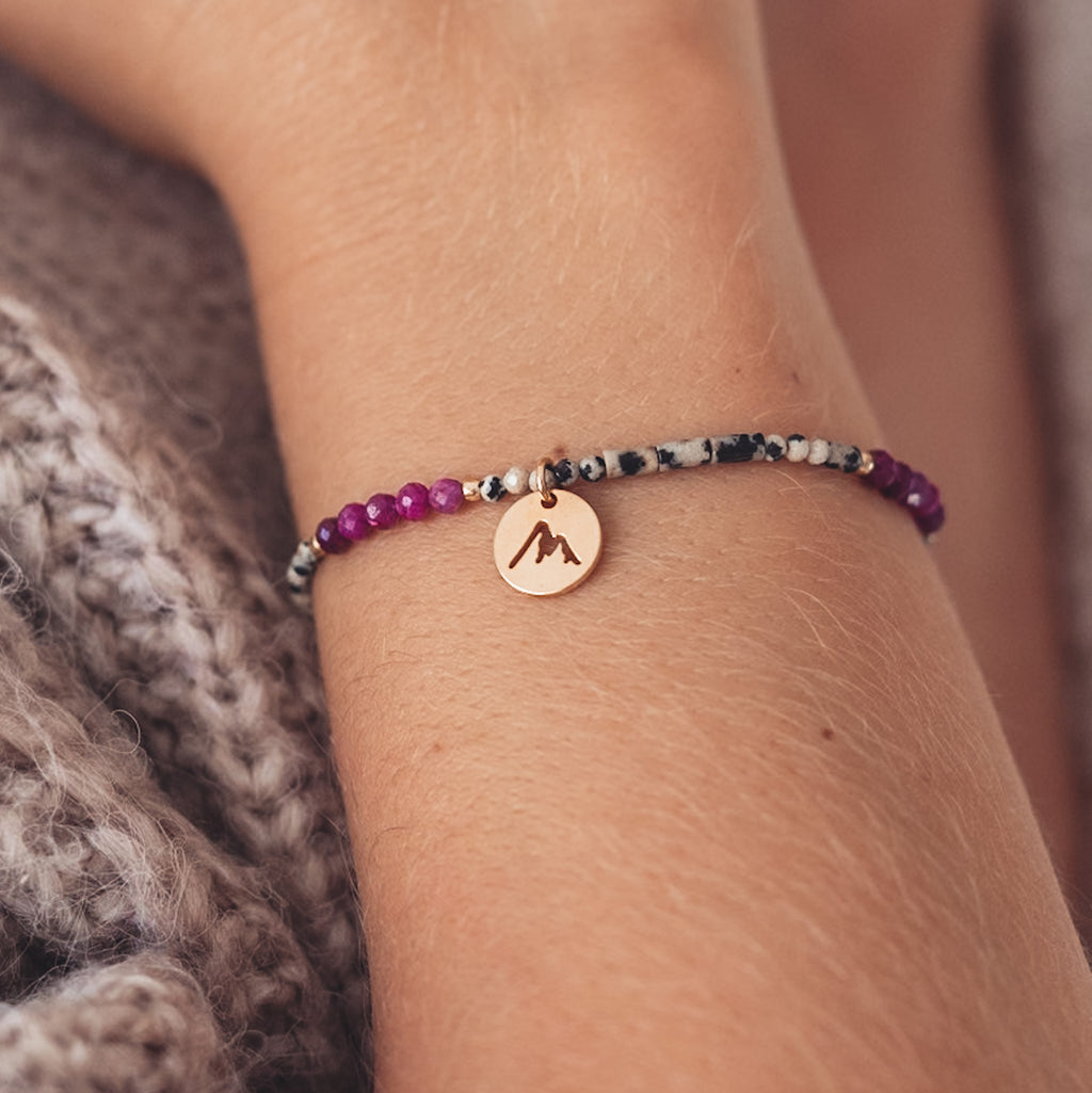 Bransoletka z dalmatyńskich i fuksjowych koralików z pozłacaną zawieszką na kobiecym nadgarstku. 