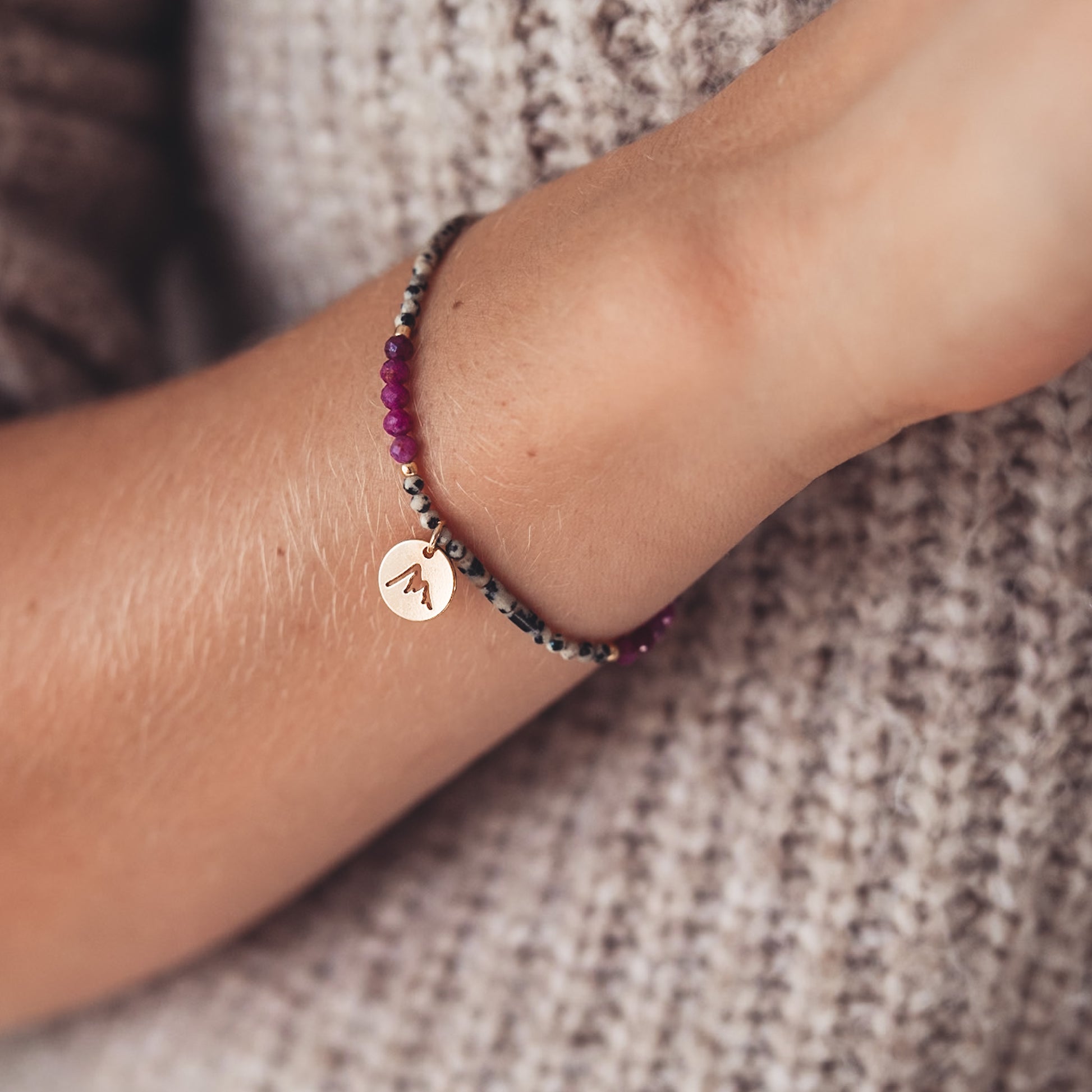 Bransoletka z dalmatyńskich i fuksjowych koralików z pozłacaną zawieszką na kobiecym nadgarstku. 