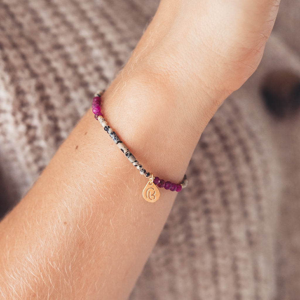 Bransoletka z dalmatyńskich i fuksjowych koralików z pozłacaną zawieszką na kobiecym nadgarstku. 