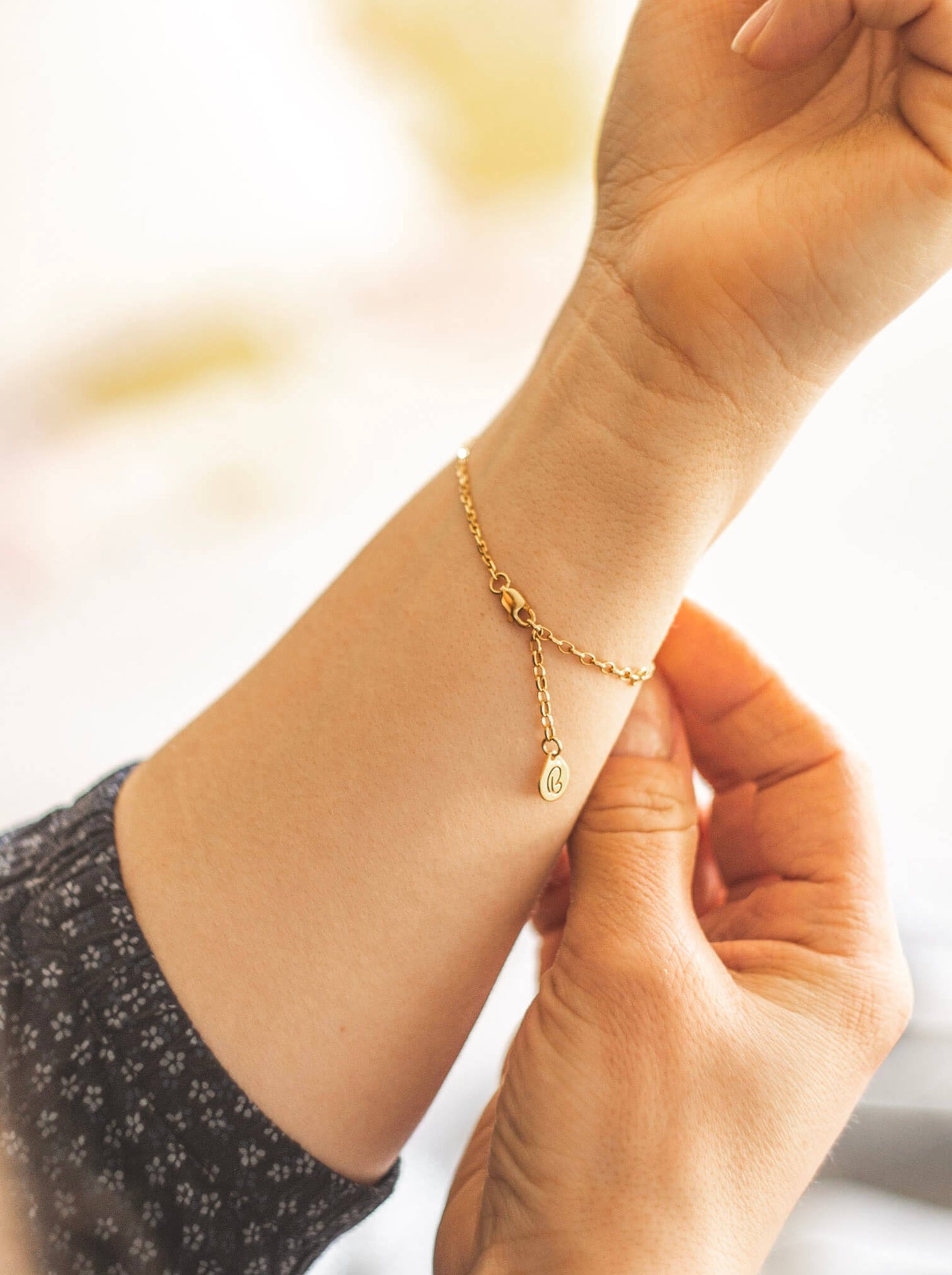 Złota bransoletka na kobiecej ręce. Zdjęcie pokazuje tylną część bransoletki. z zapięciem i zawieszką z logo marki Believy.